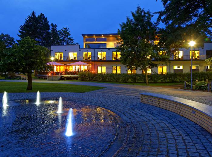 Hotel am Kurpark Zinnowitz am Abend mit beleuchteter Terrasse und Springbrunnen im Kurpark