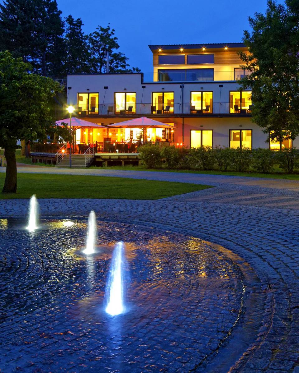 Hotel am Kurpark Zinnowitz am Abend mit beleuchteter Terrasse und Springbrunnen im Kurpark